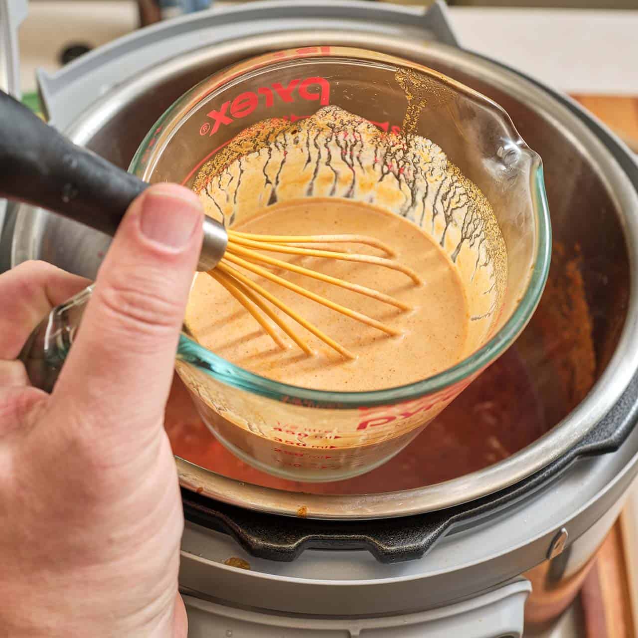 A measuring cup full of whisked sour cream and pot liquid