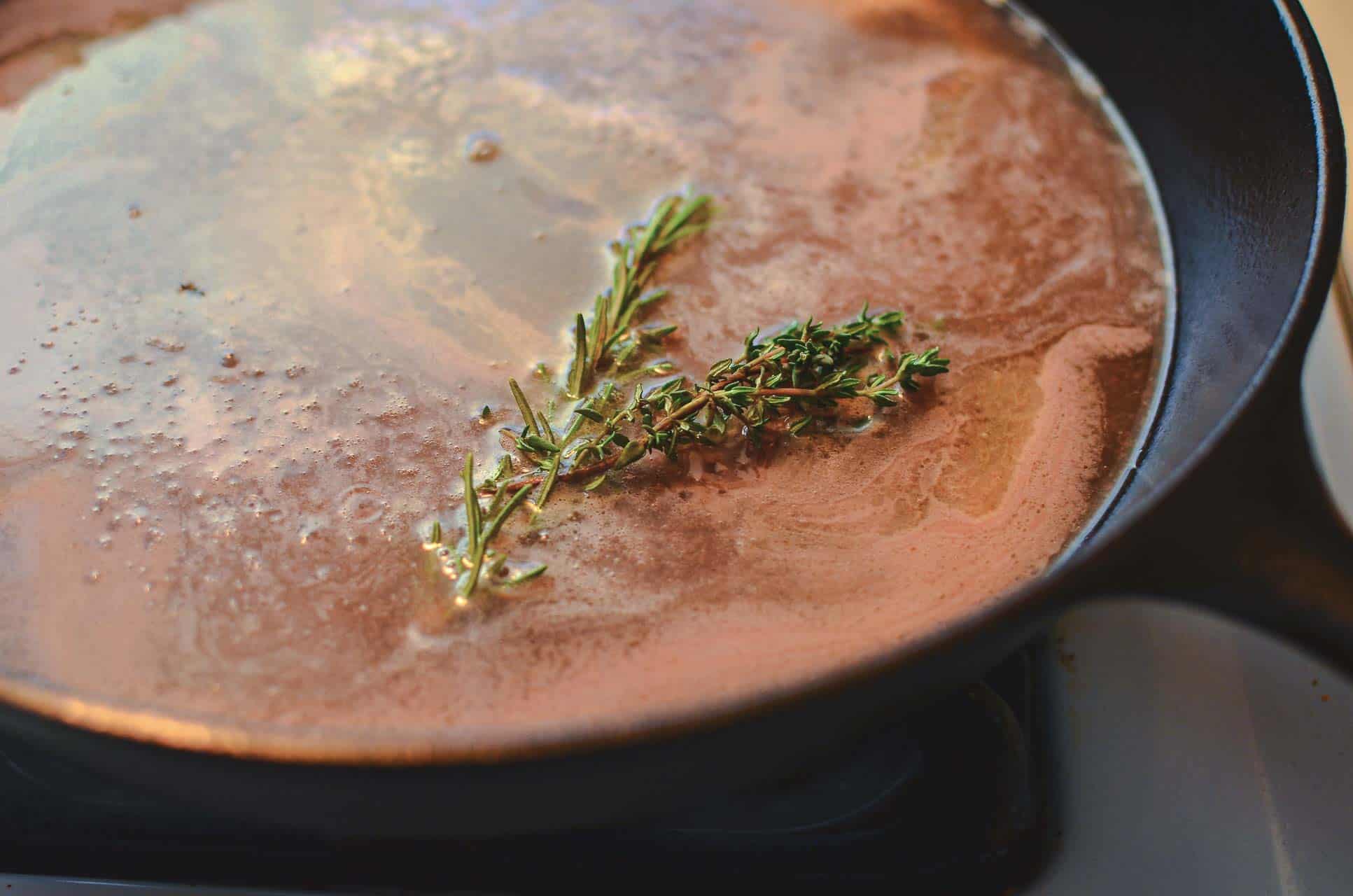 A pan with a thin layer of broth and sprigs of fresh thyme and parsley