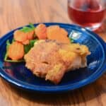 Cooked chicken thighs on a plate with vegetables, with a glass of wine.