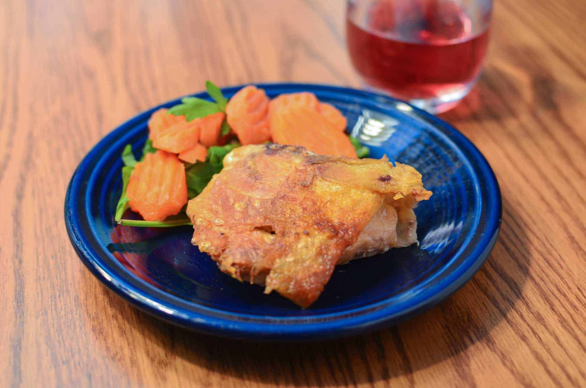 Cooked chicken thighs on a plate with vegetables, with a glass of wine.