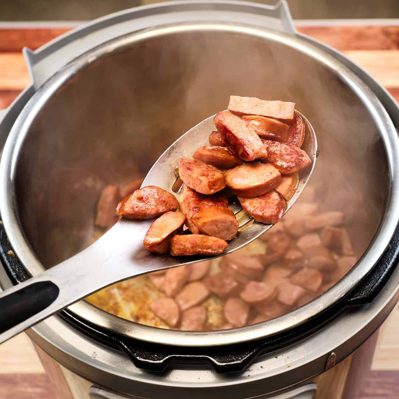 Browned sausage in a slotted spoon over an instant pot