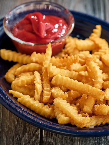 A platter of crinkle cut french fries with a bowl of ketchup