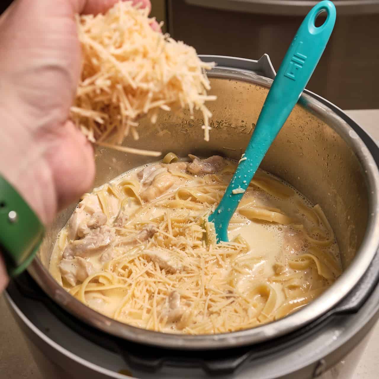 Sprinkling cheese into an Instant Pot full of fettuccine alfredo