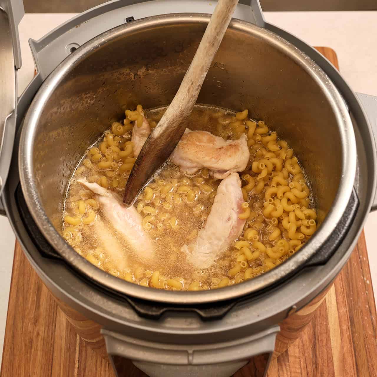 An Instant Pot with noodles, broth, and chicken ready to cook