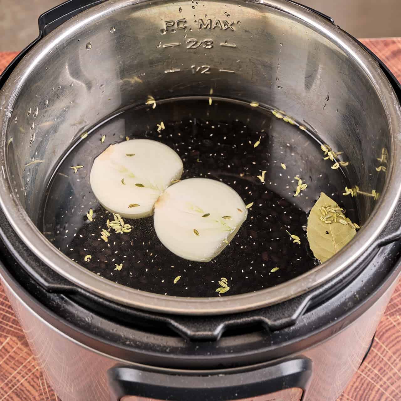Instant Pot with black beans, onion, bay leaf, fennel, and water, ready to cook