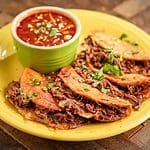 A plate of birria tacos with broth