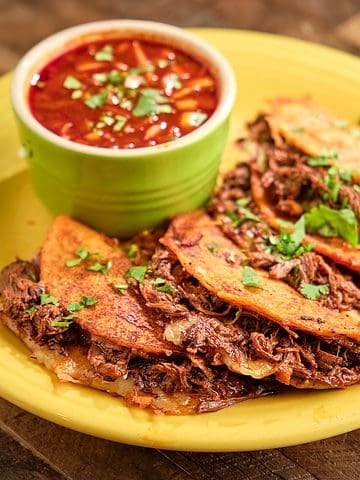 A plate of birria tacos with broth