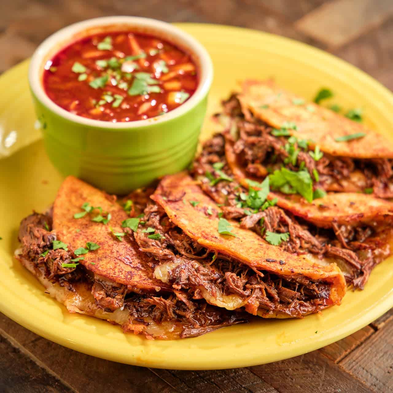 A plate of birria tacos with broth