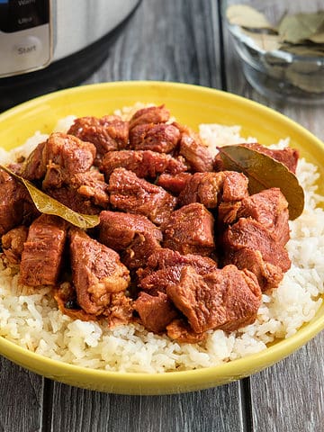 A bowl of Pork Adobo with bay leaves on a bed of rice