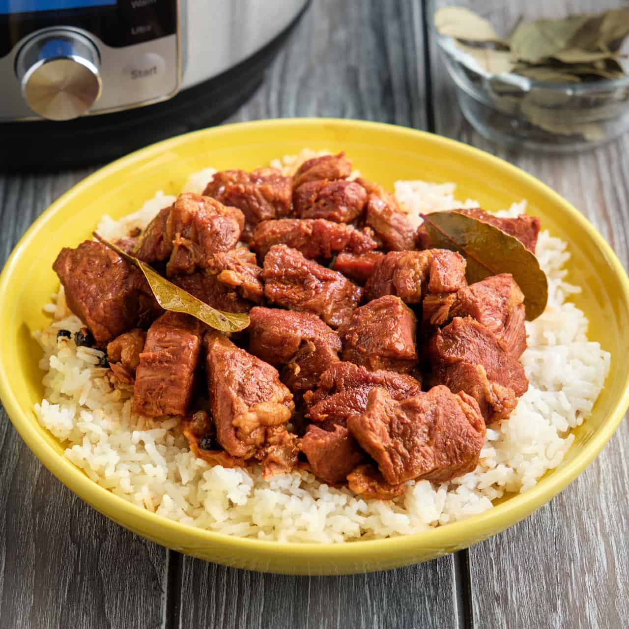 A bowl of Pork Adobo with bay leaves on a bed of rice