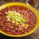 A bowl of venison chili with pinto beans topped with shredded cheddar and green onions