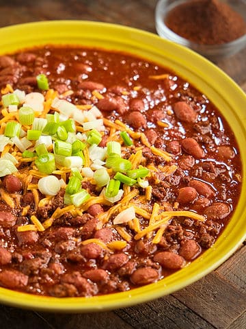 A bowl of venison chili with pinto beans topped with shredded cheddar and green onions