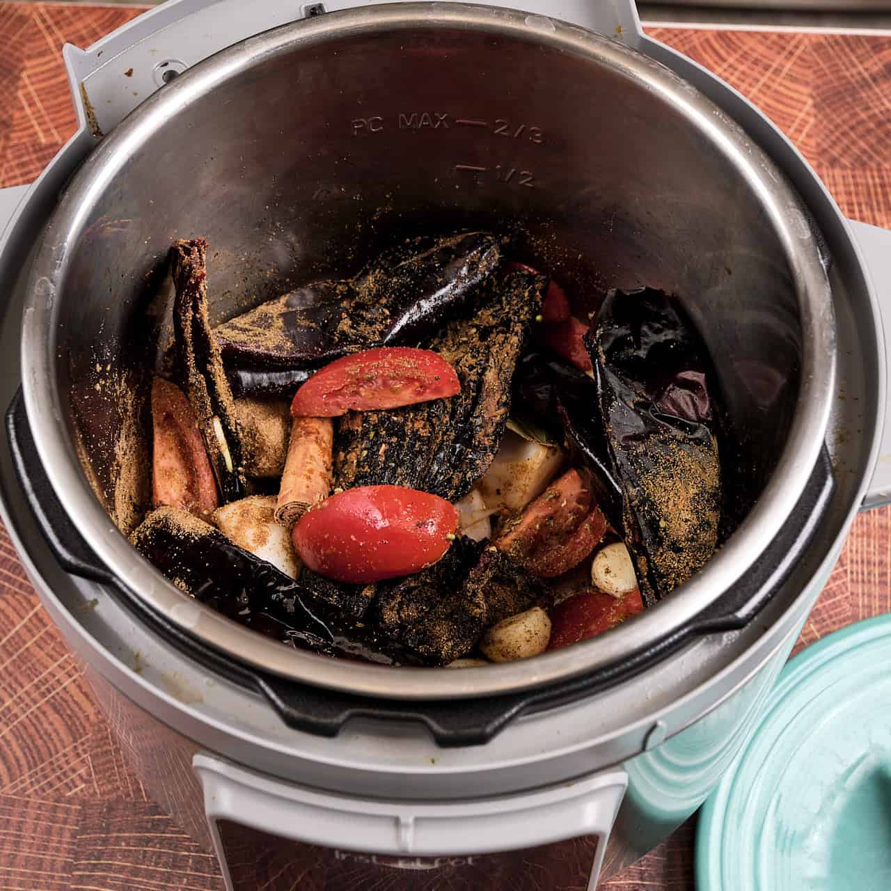 An instant pot with dried chiles, onions, garlic, tomatoes, and spices