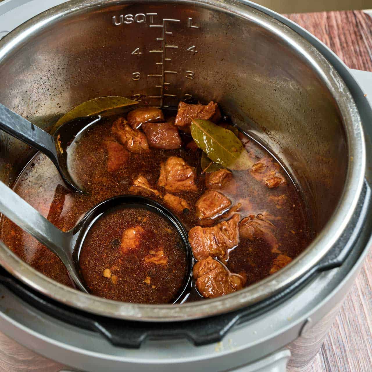An Instant Pot with a ladle scooping cooked pork adobo and its liquid