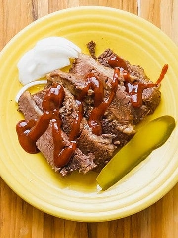 A plate of brisket slices with a pickle, onion, and bbq sauce