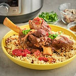 A lamb shank on a bowl of couscous with an Instant Pot in the background