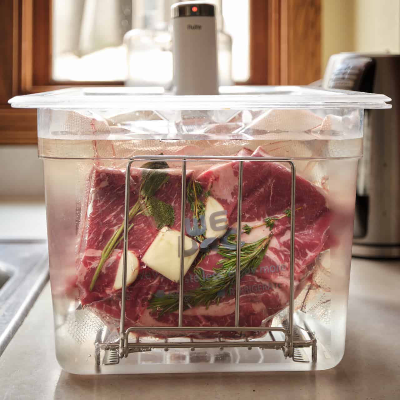 Vacuum bag of chuck steak and herbs in a sous vide water bath