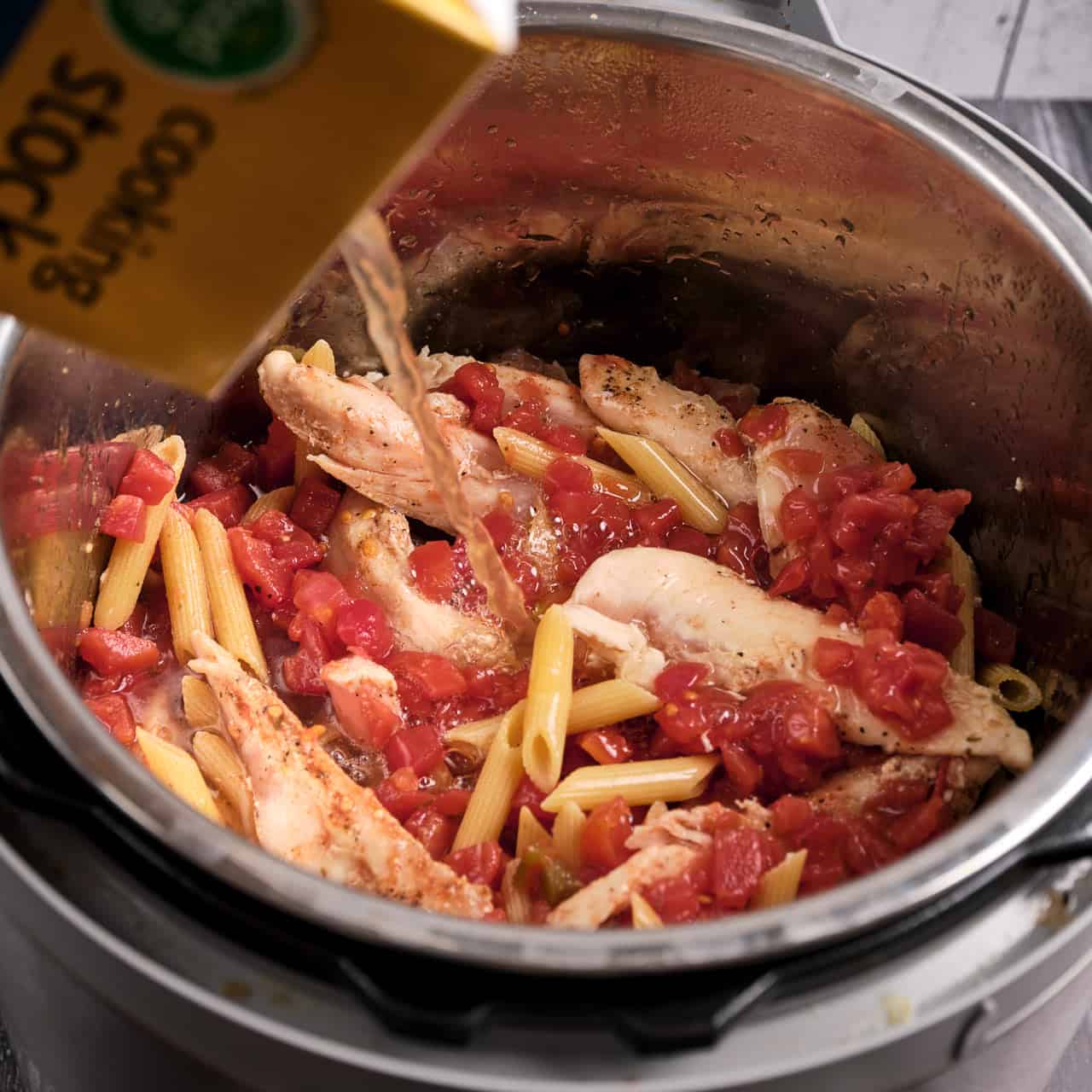 Pouring chicken broth over the penne, chicken, and tomatoes