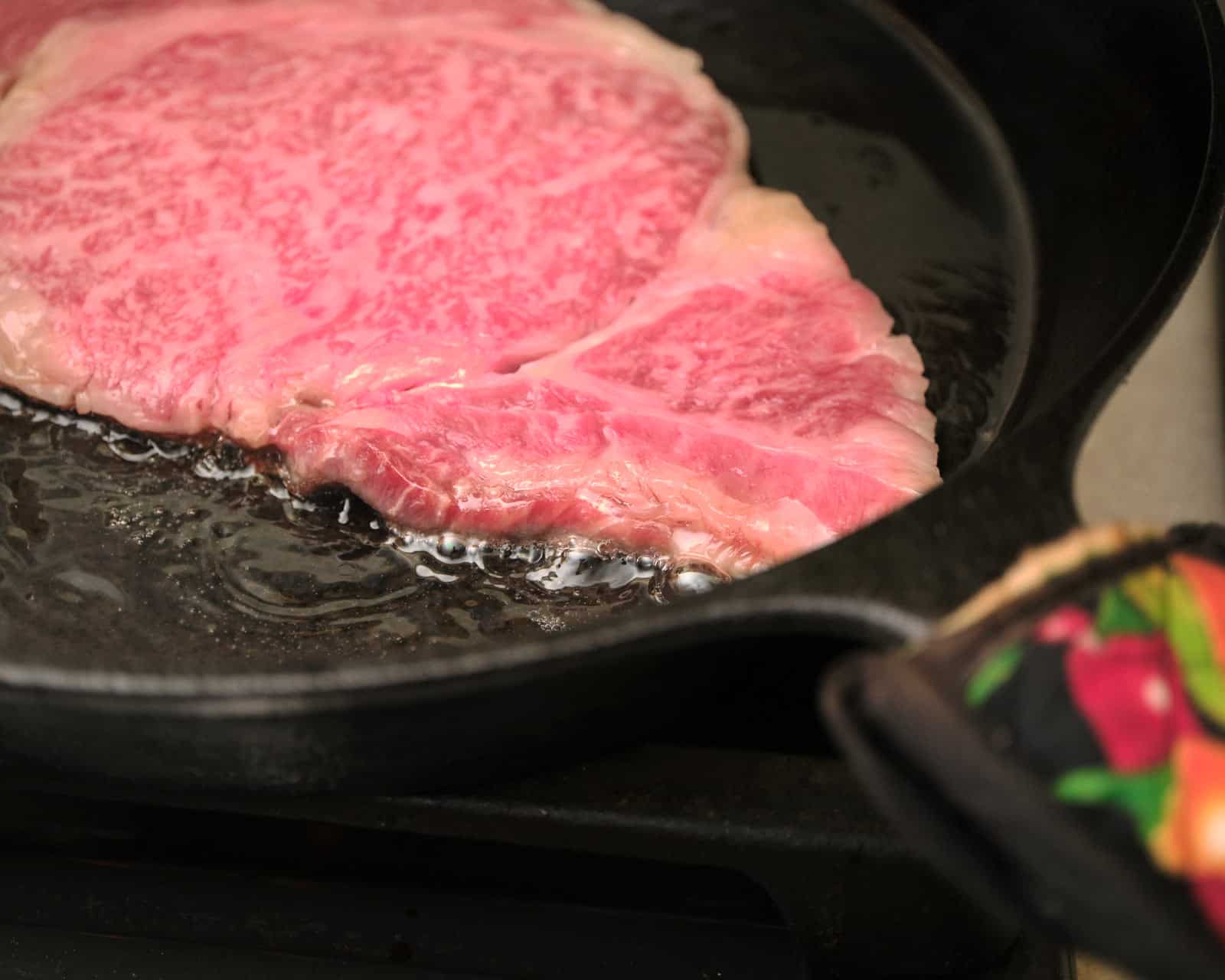 Fat escaping from a wagyu ribeye in the pan