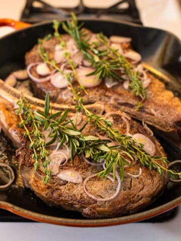 Ribeye Steaks in Cast Iron Pan covered with Herbs and Shallots