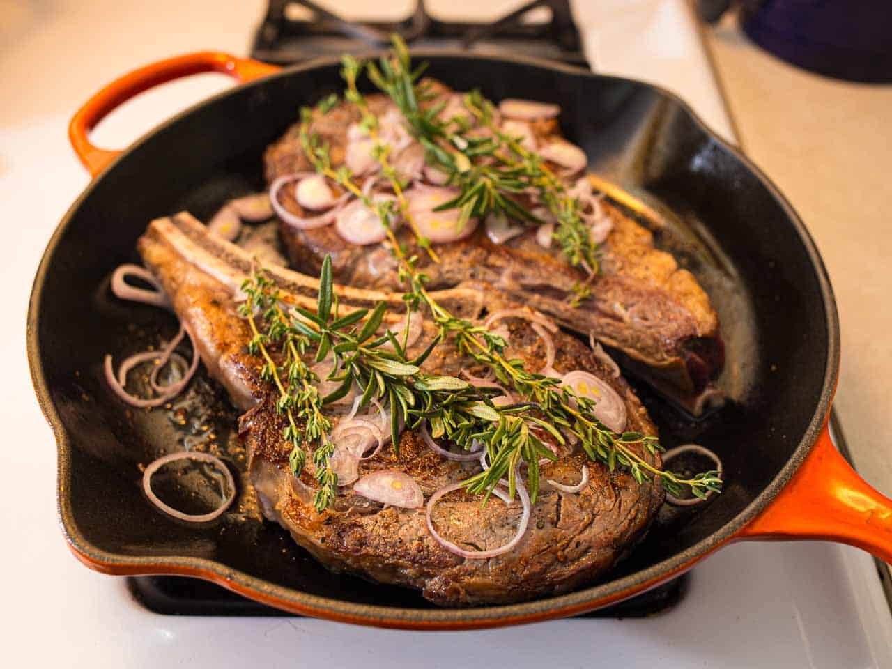 Ribeye Steaks in Cast Iron Pan covered with Herbs and Shallots