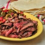 A platter of beef fajitas, peppers, and onions, with tortillas in the background