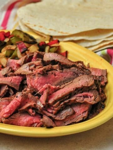 A platter of beef fajitas, peppers, and onions, with tortillas in the background