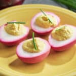 Beet pickled deviled eggs topped with a piece of chive