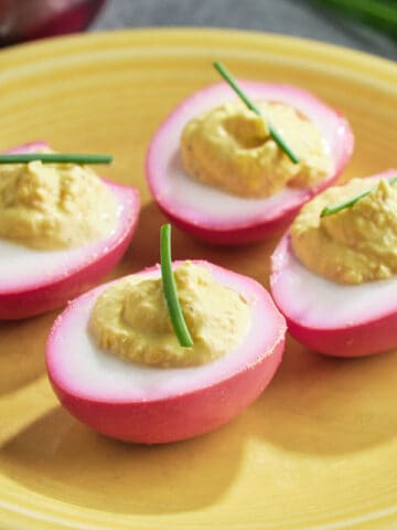 Beet pickled deviled eggs topped with a piece of chive