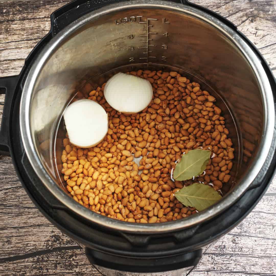 An Instant Pot full of dry buckeye beans, with onions an bay leaves