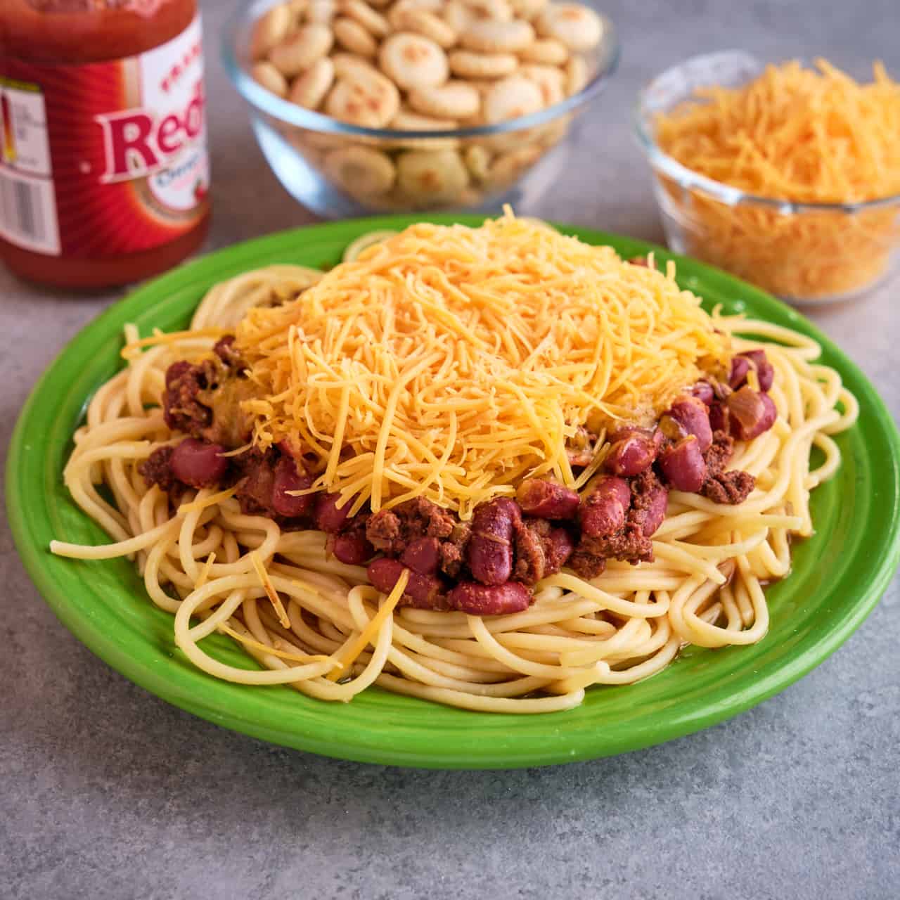 A plate of Cincinnati chili with cheese, oyster crackers, and hot sauce