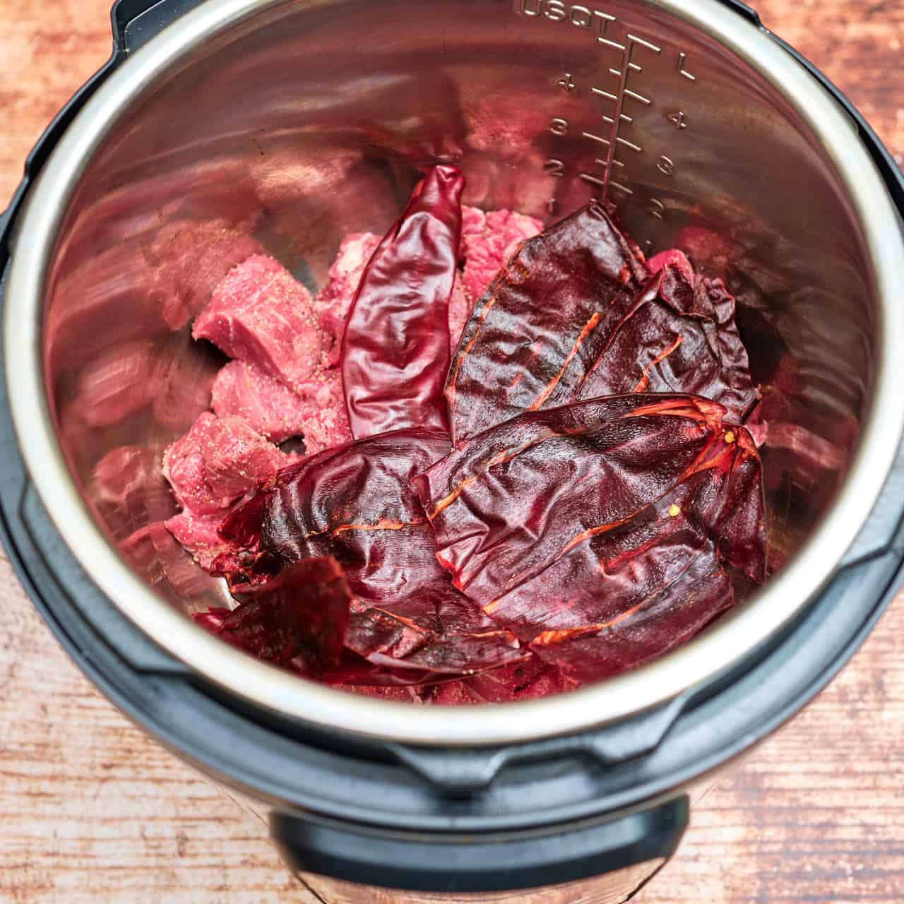 Guajillo peppers on top of pork cubes in an Instant Pot