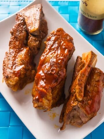 Boneless pork ribs on a white platter with jars of BBQ rub and BBQ sauce