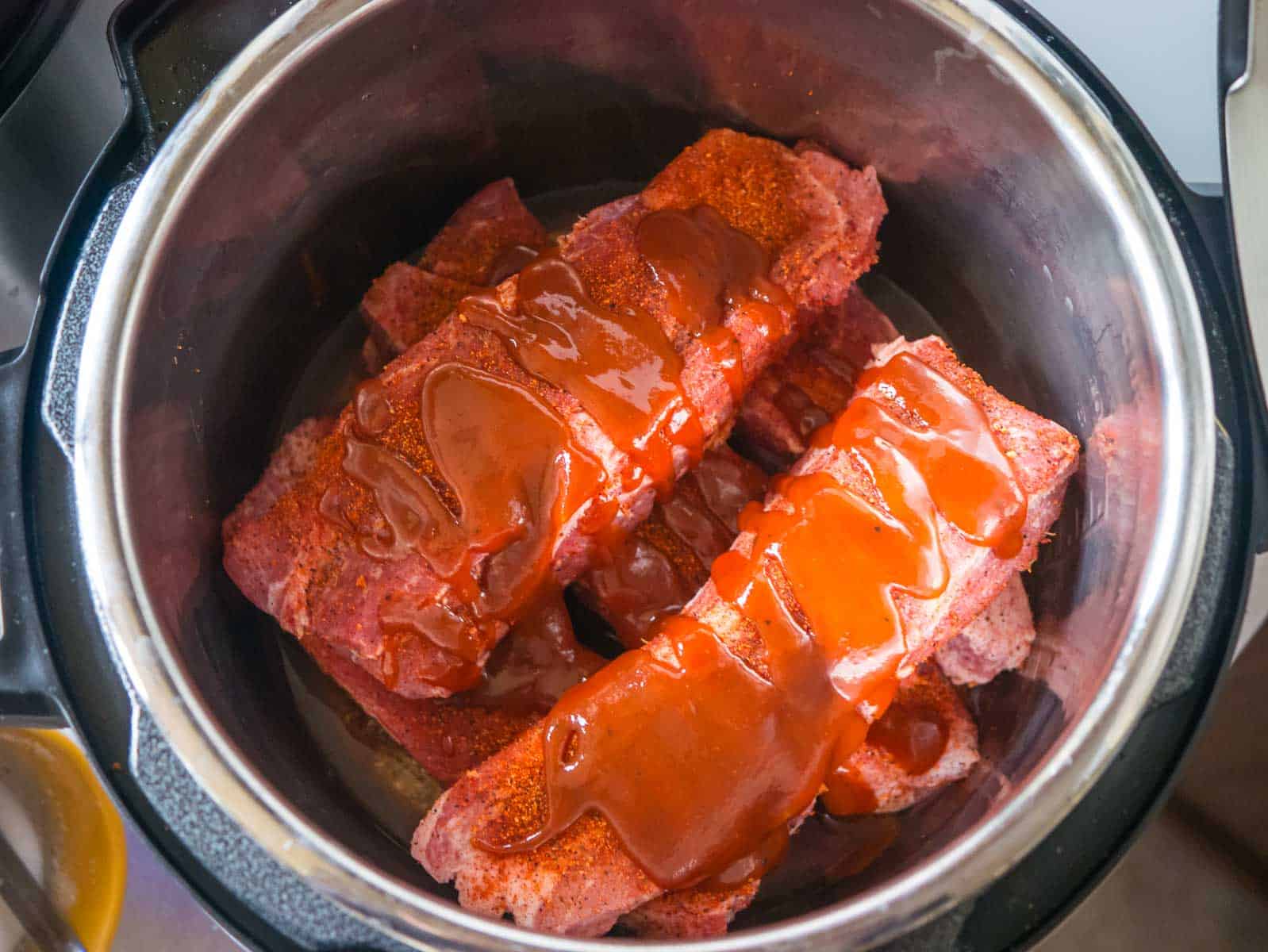 Boneless ribs stacked in an Instant Pot with BBQ sauce on top