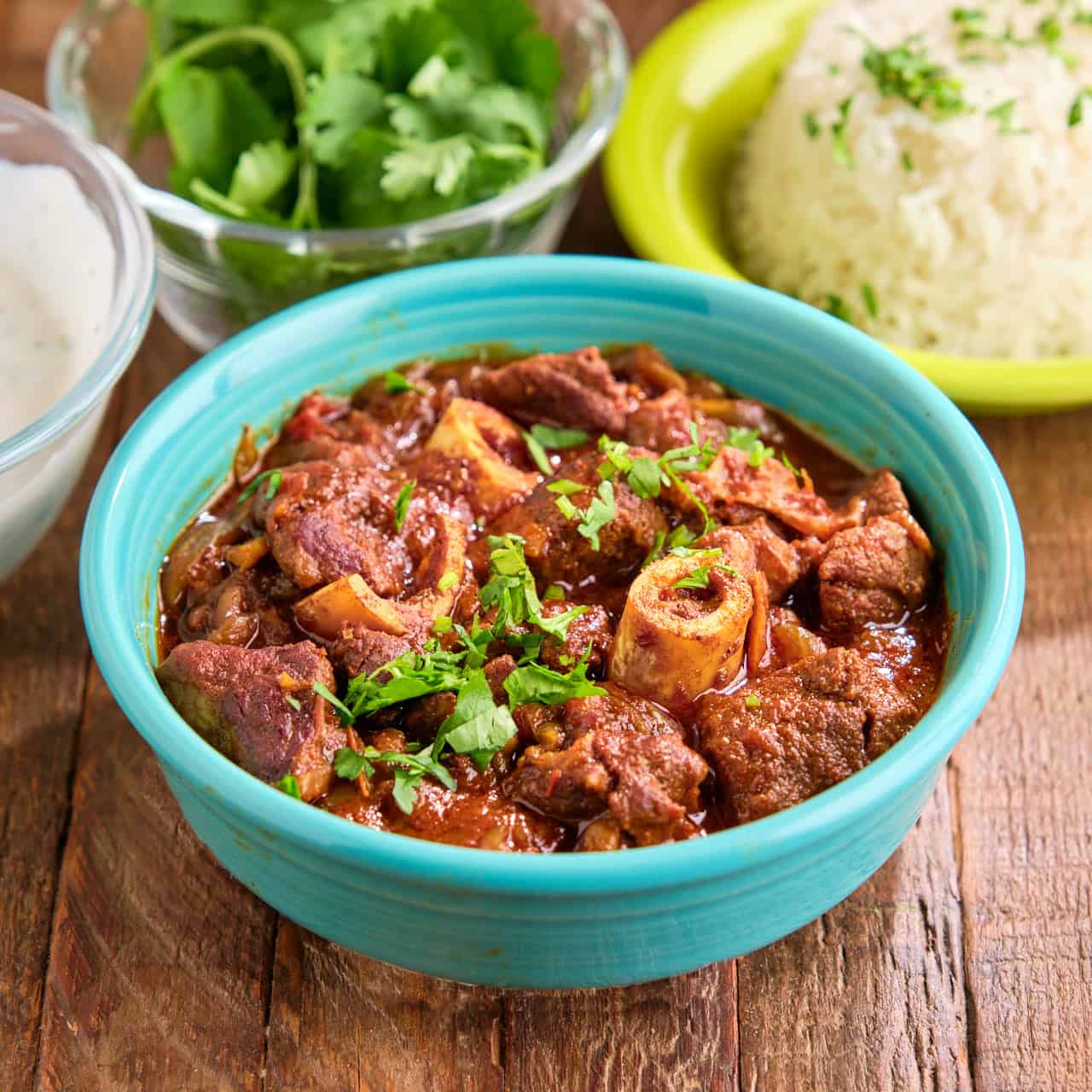 A bowl of Instant Pot Goat Curry with cilantro and rice in the background