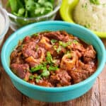 A bowl of Instant Pot Goat Curry with cilantro and rice in the background