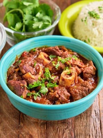 A bowl of Instant Pot Goat Curry with cilantro and rice in the background