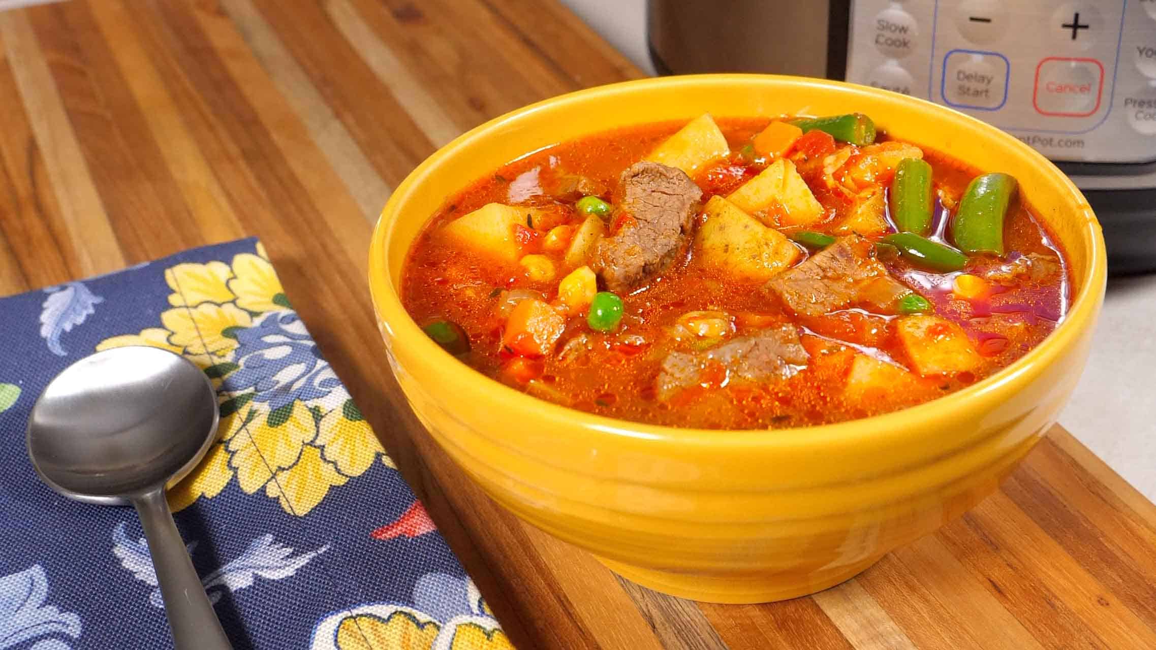 A bowl of Instant Pot Vegetable Beef soup, with an Instant Pot in the background