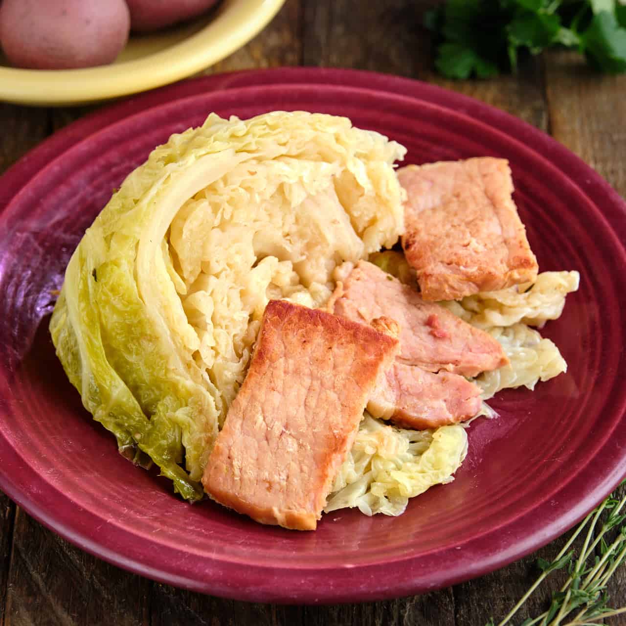 A plate of instant pot cabbage with bacon and butter, with herbs and potatoes in the background