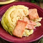A plate of instant pot cabbage with bacon and butter, with herbs and potatoes in the background