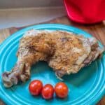 Cooked chicken leg on a plate with cherry tomatoes with a pinch mitt in the background