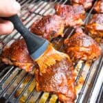 Brushing a row of bbq chicken thighs with more sauce