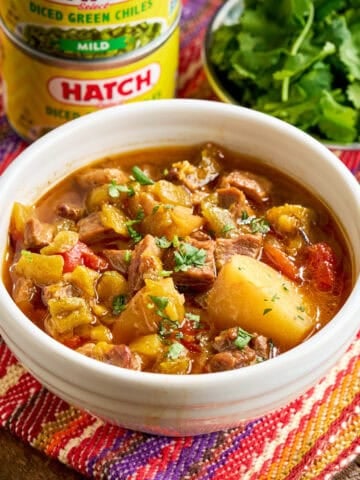 A bowl of Instant Pot Green Chile Stew with minced cilantro and cans of hatch chiles
