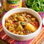 A bowl of Instant Pot Green Chile Stew with minced cilantro and cans of hatch chiles