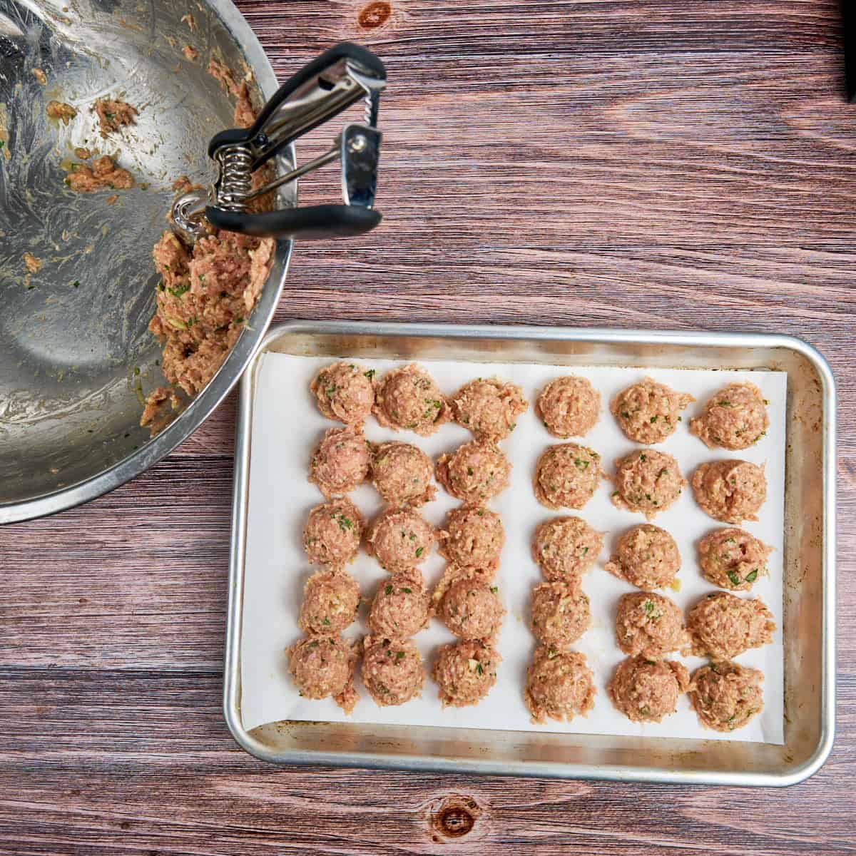 A tray of small meatballs with the bowl and cookie scoop