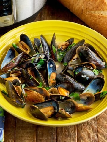 A bowl of Instant Pot Mussels with a loaf of bread and an Instant Pot in the background