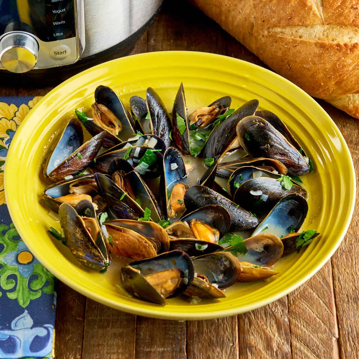 A bowl of Instant Pot Mussels with a loaf of bread and an Instant Pot in the background