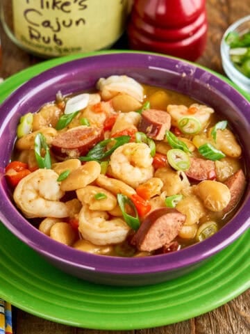 A bowl of Instant Pot Butter Beans and Shrimp with seasoning, hot sauce, and minced green onions