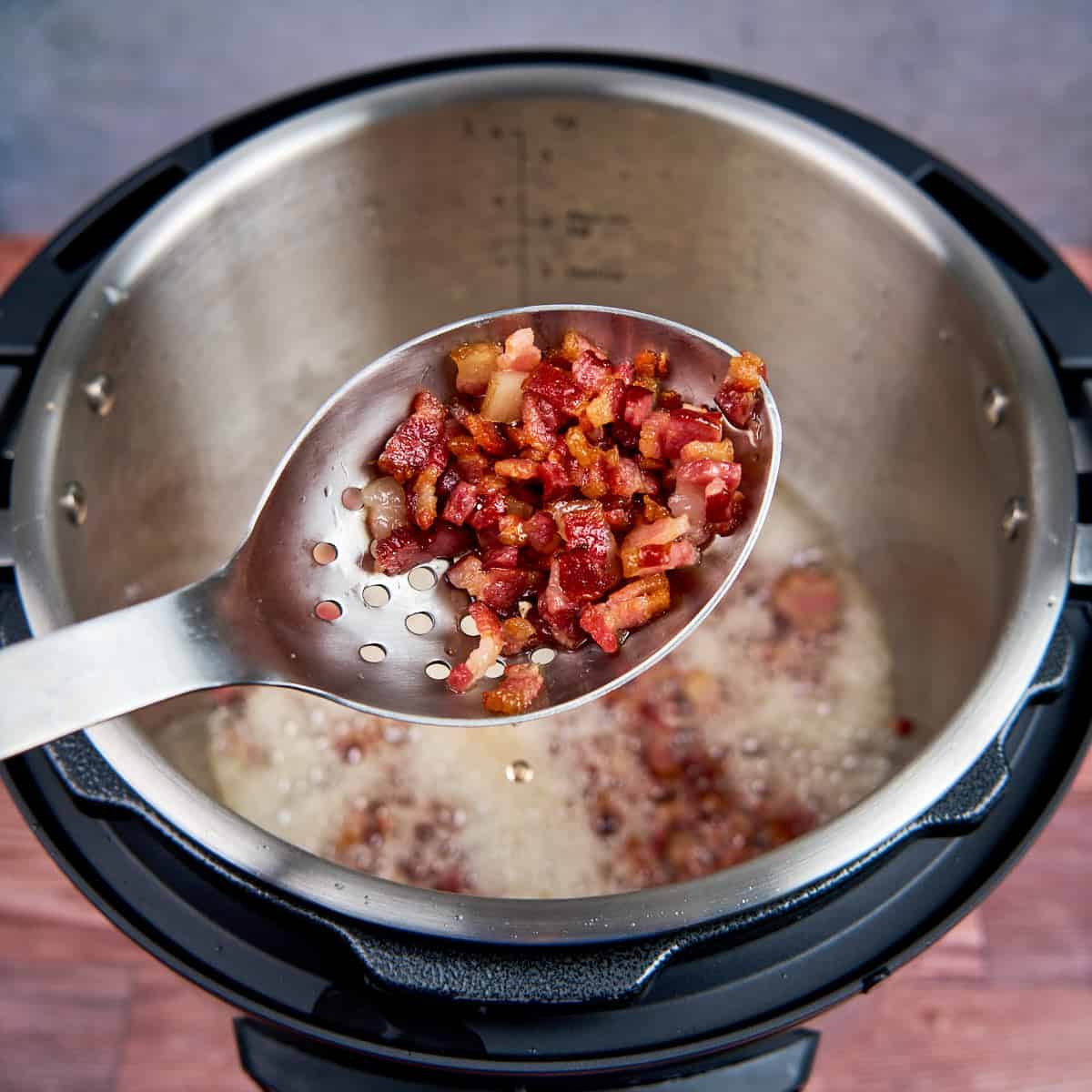 A slotted spoon full of browned bacon