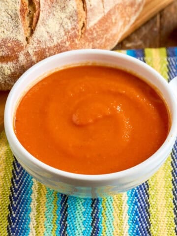 A bowl of Instant Pot Tomato Soup with a spoon and a loaf of bread